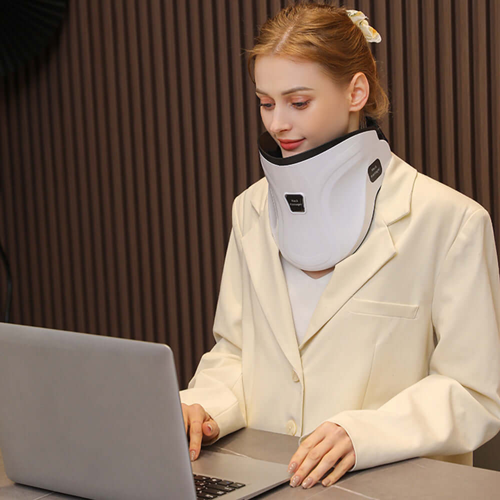 Woman wearing an electric neck massager with heat and air traction while working on a laptop.